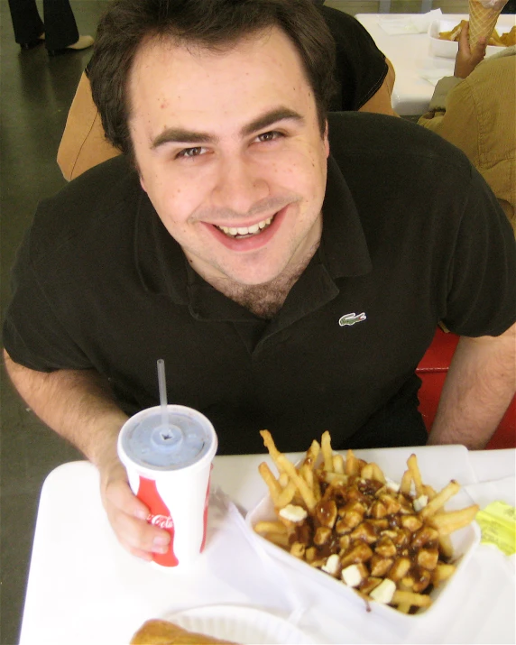 man smiling and holding a beverage over a tray of food