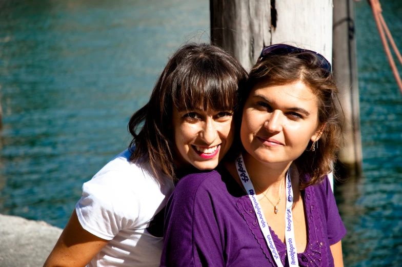 two women are standing together by a body of water