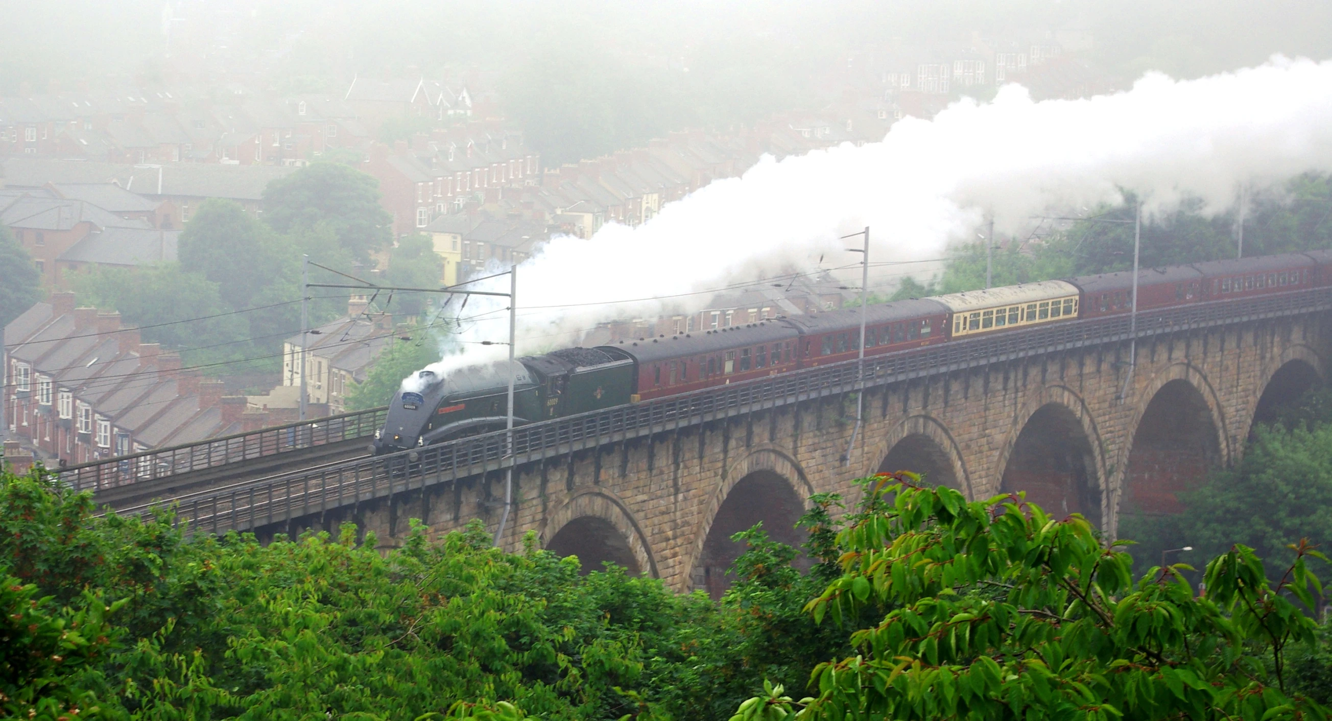 a steam train coming down the track on the train bridge