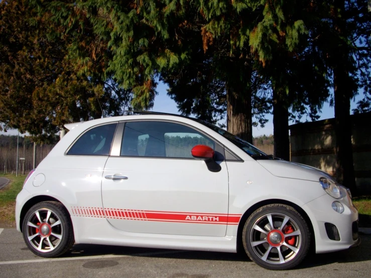 a small white car with red trims sits parked next to trees