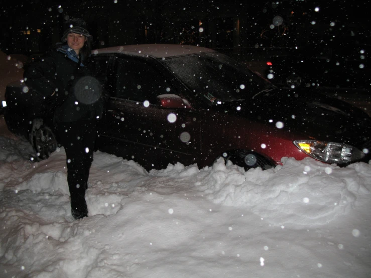 a woman standing on a snow covered sidewalk next to a parked car