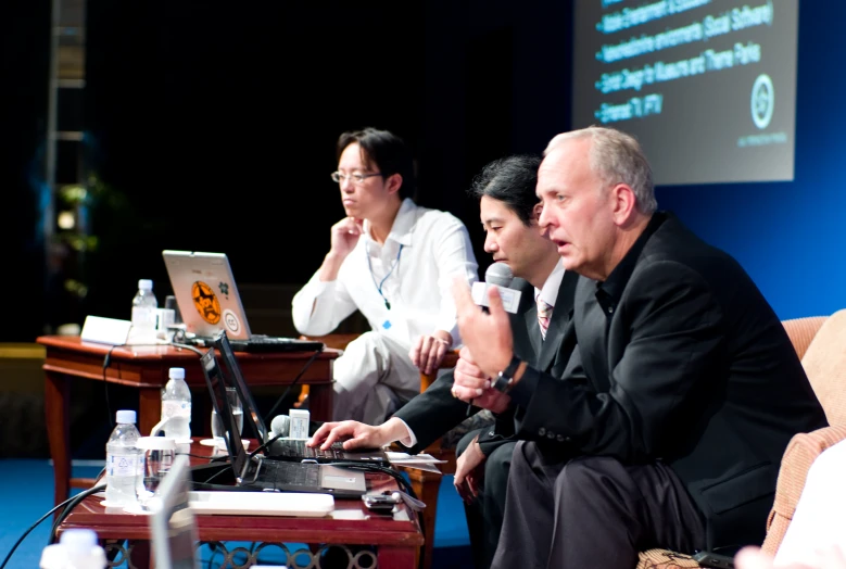 three men on a couch are looking at a laptop