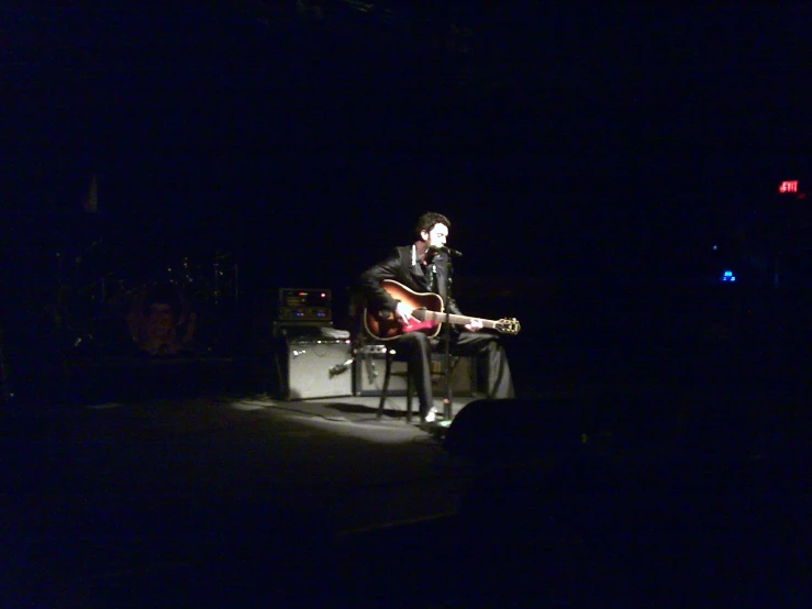 a person sitting on a chair in the dark with his legs crossed