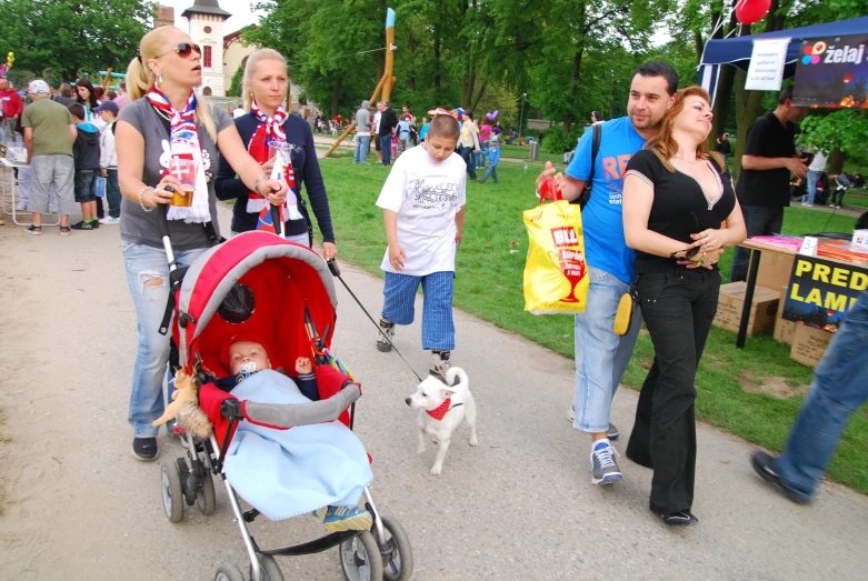 a group of people walking in the park with a baby in a stroller