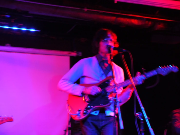 a man holding a guitar in front of a microphone and standing on stage