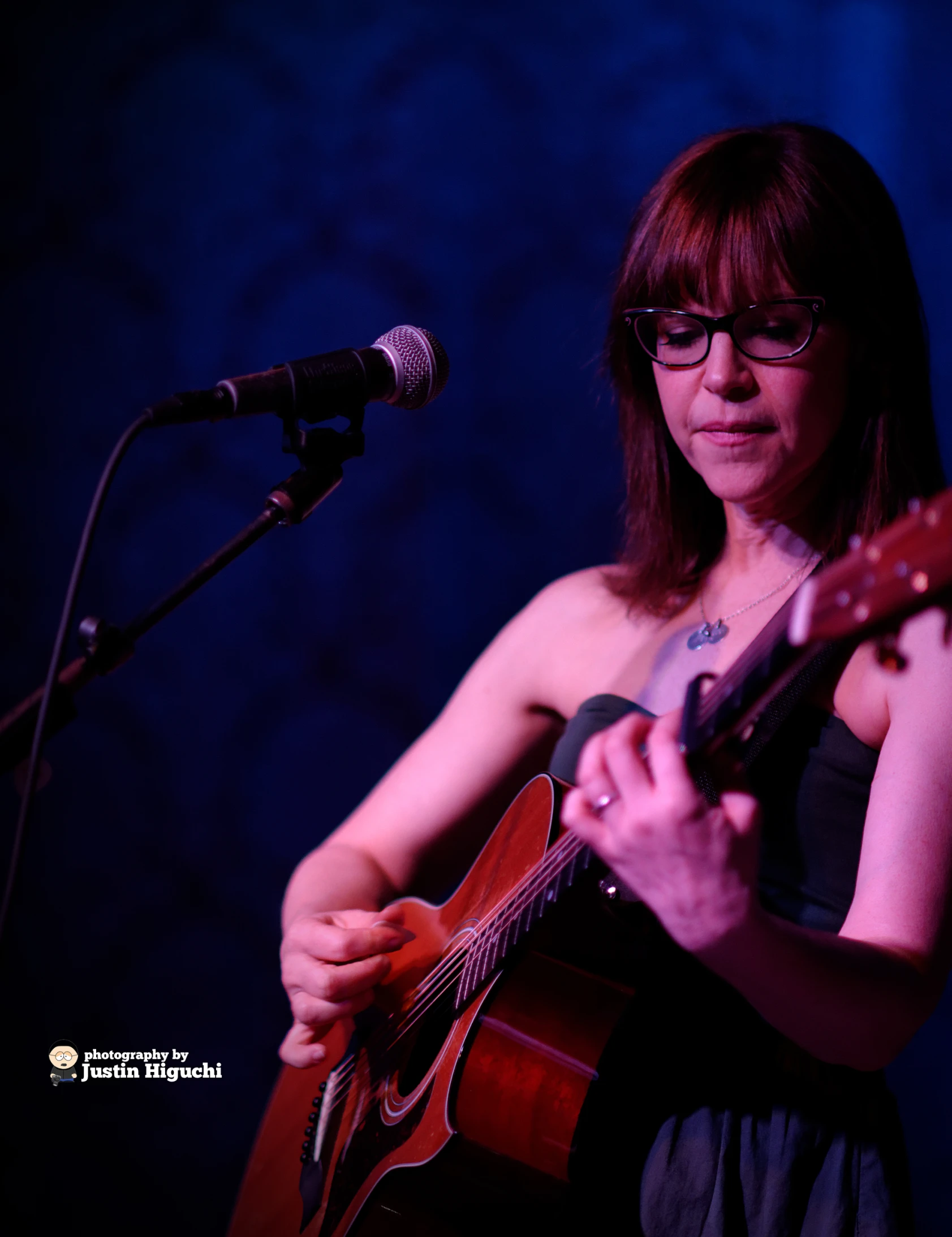 a woman playing an acoustic guitar at a microphone