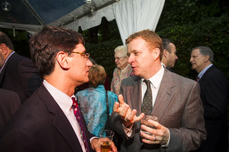 two men dressed in suits are drinking alcohol at a party