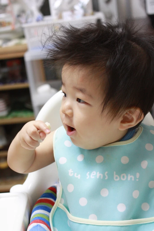 baby with bib chewing on food in high chair