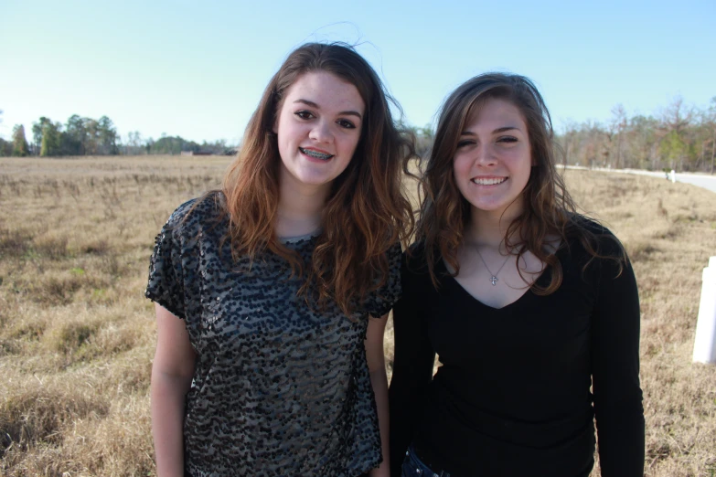 two young women stand near a field on a sunny day