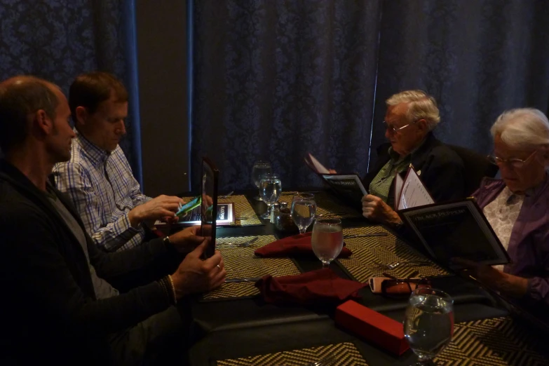 four people sitting at a table looking at their electronic devices