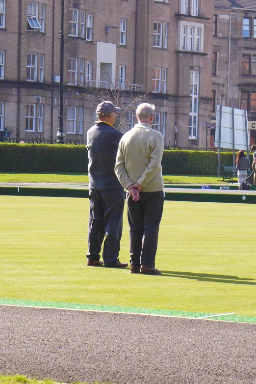 two men stand on the grass near some brown building