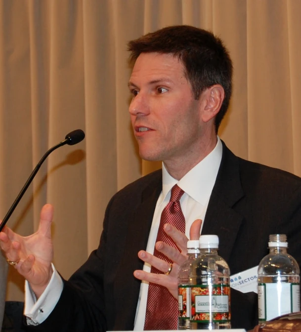 a man giving a speech while sitting at a desk