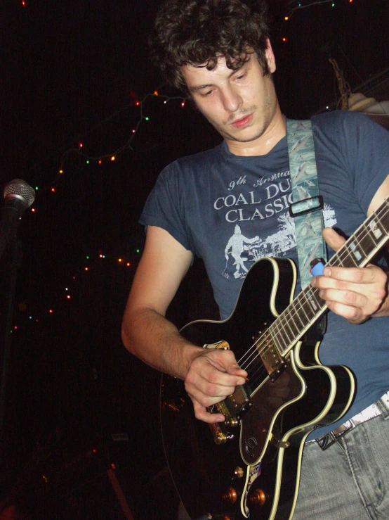 young adult playing electric guitar in front of christmas lights