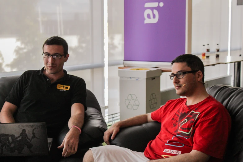 two men are sitting down on a black chair