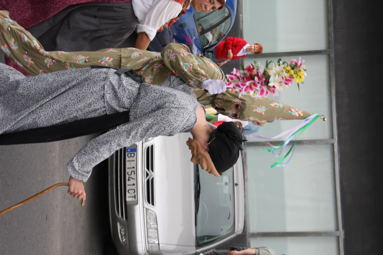 two people dressed in costumes walking with a stick in a city street