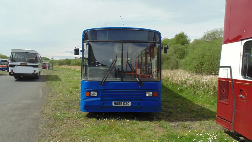 a blue bus sits parked in a grassy area next to a road