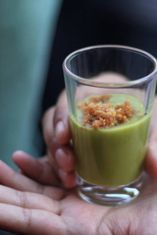 a person is holding a glass with some green liquid