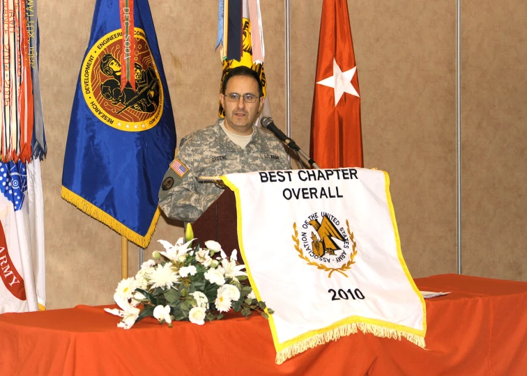 a man wearing uniform is standing in front of flags and microphone