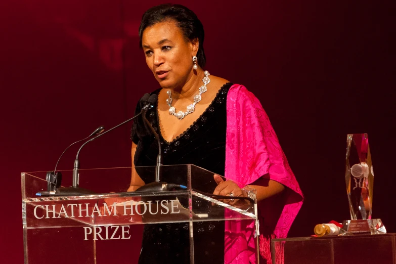 a woman standing at a podium in front of a red wall