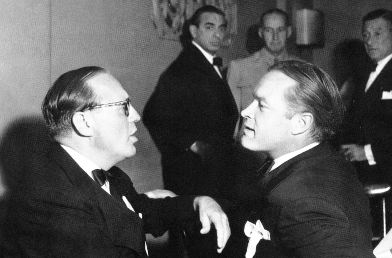 two men in suits talking to each other while others watch