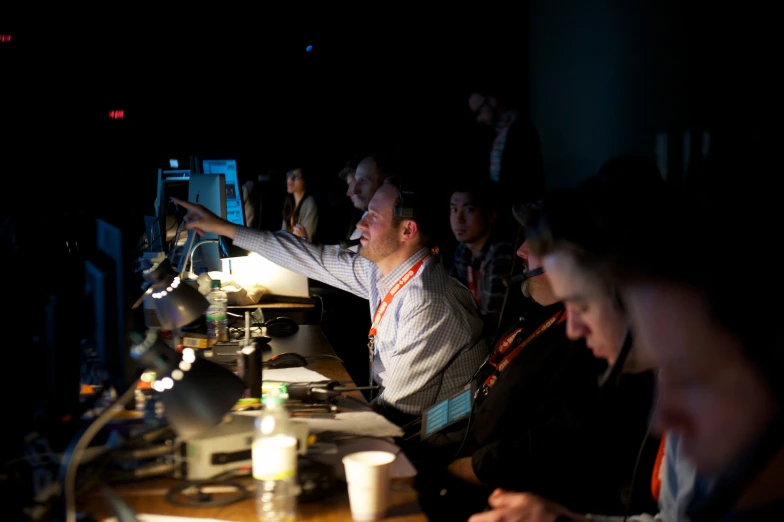 a group of men sitting around computers in a room