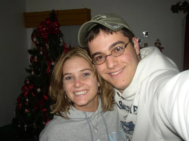 the man and woman are standing by a christmas tree