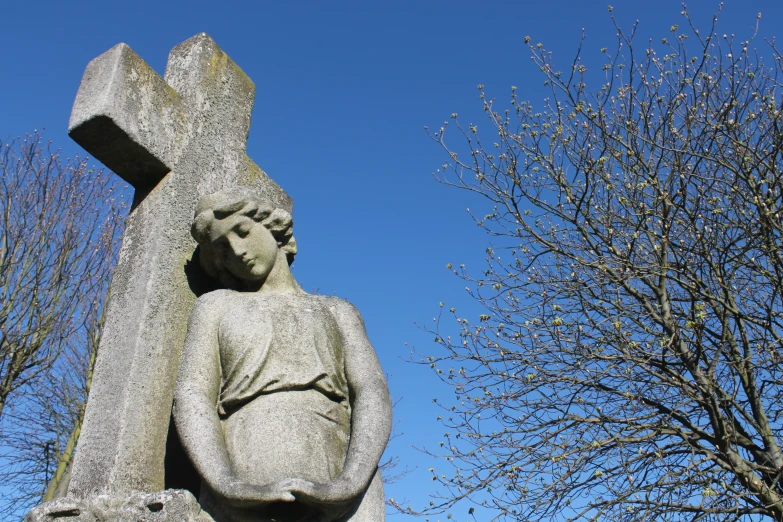 a statue of a female holding a cross next to a tree