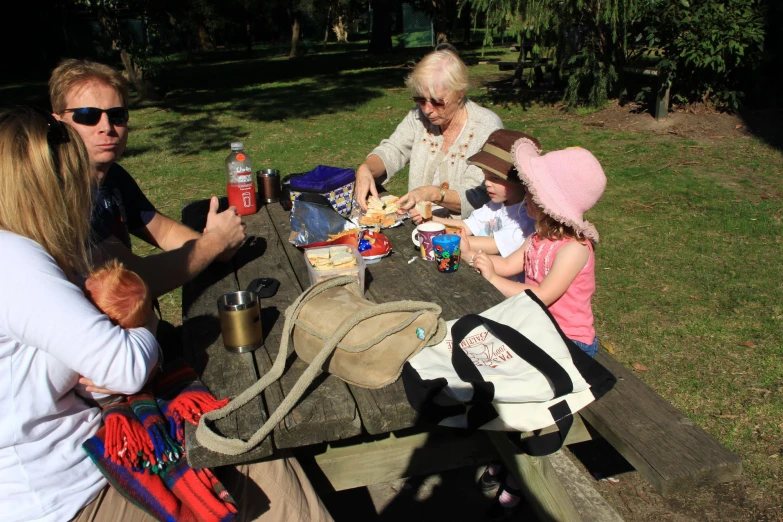 four people sit at an outdoor picnic table while eating food