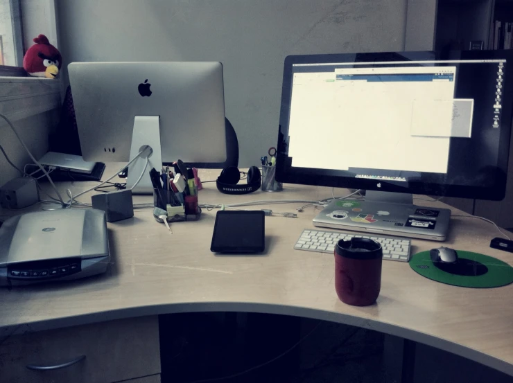 a desk with three computers and a printer