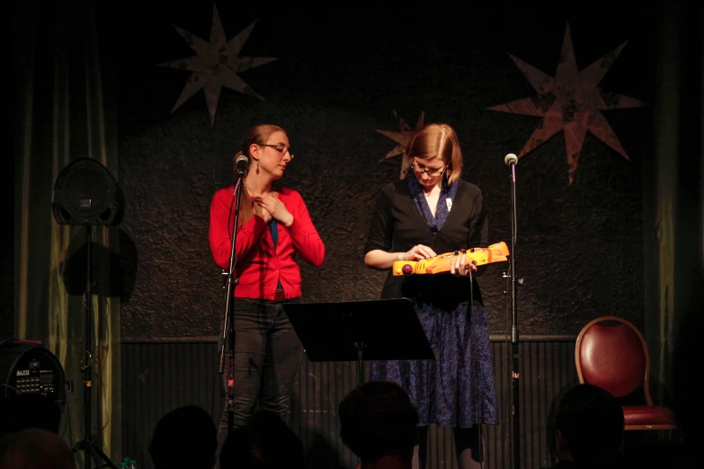 two women standing on stage and singing at the microphone