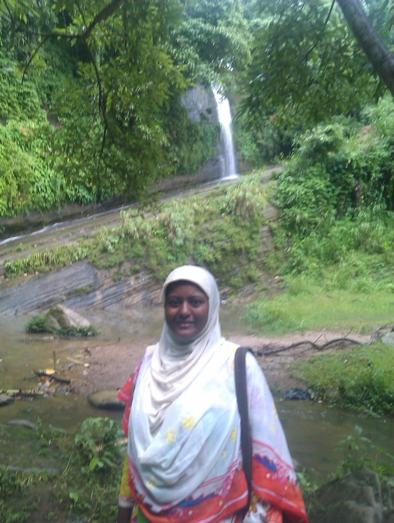 an indian woman poses in front of a waterfall