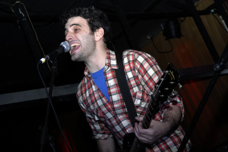 man in plaid shirt singing and holding a guitar