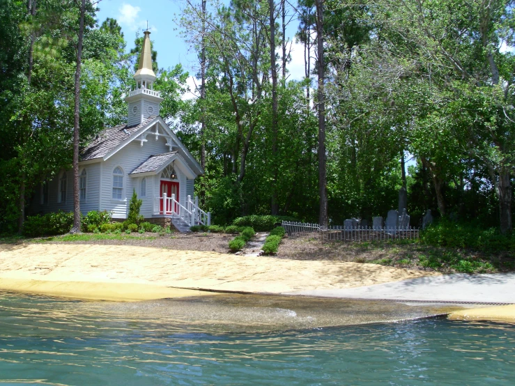 a white church sits at the edge of a lake in front of trees