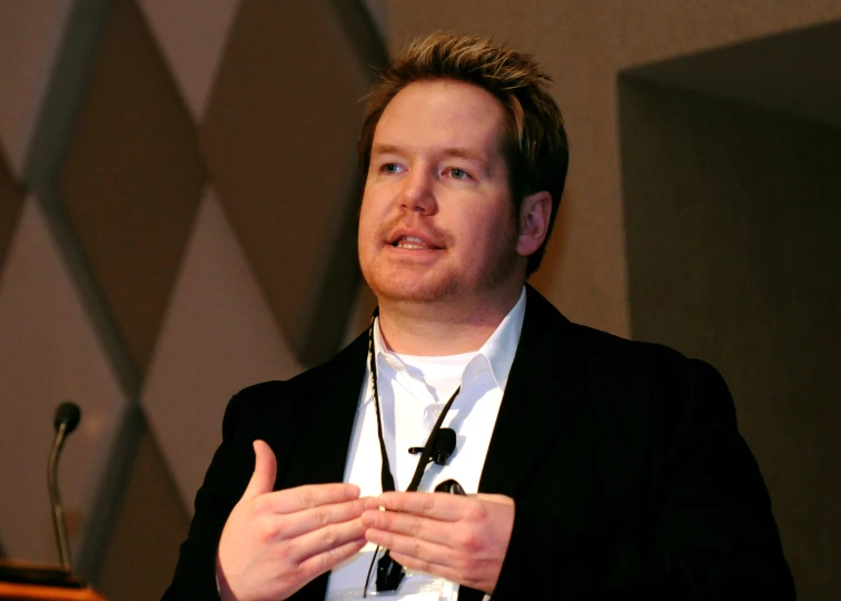 a man in black jacket and white shirt talking to a crowd