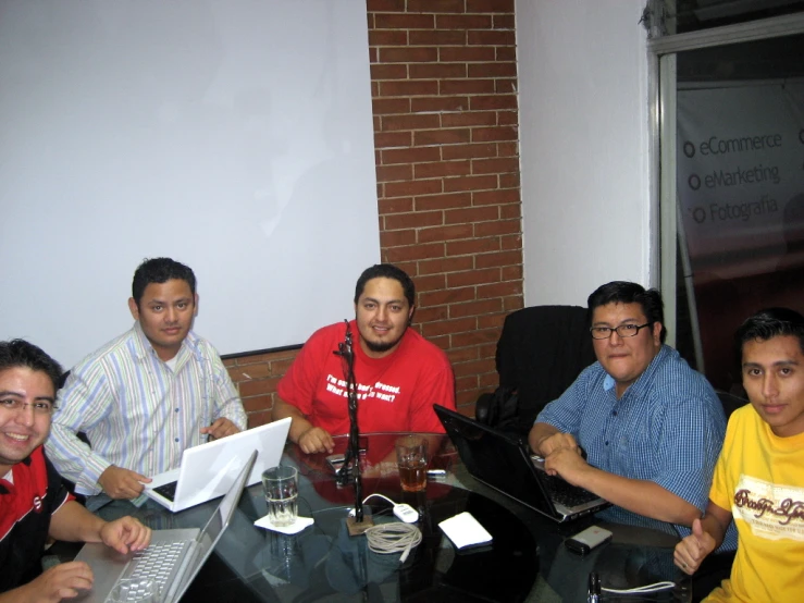 five men around a table with two of them holding laptops