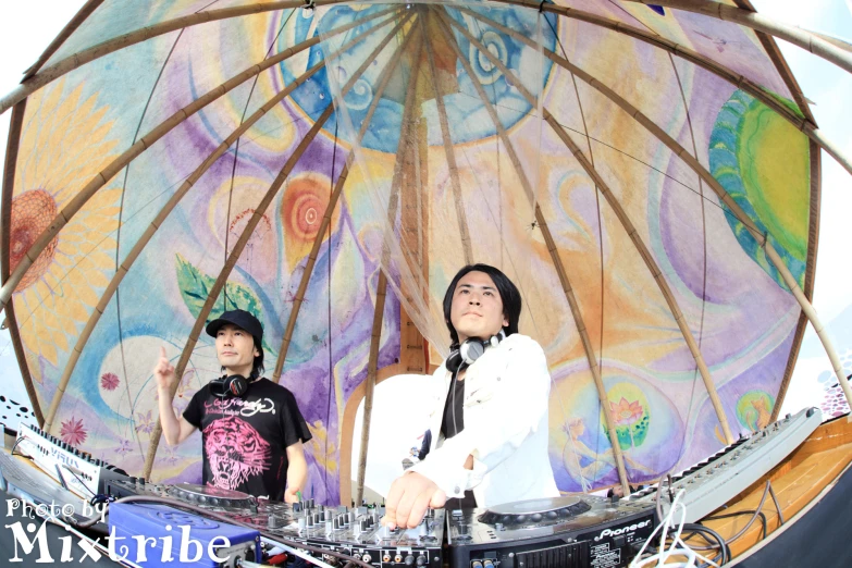 two djs standing under a large umbrella at a music concert