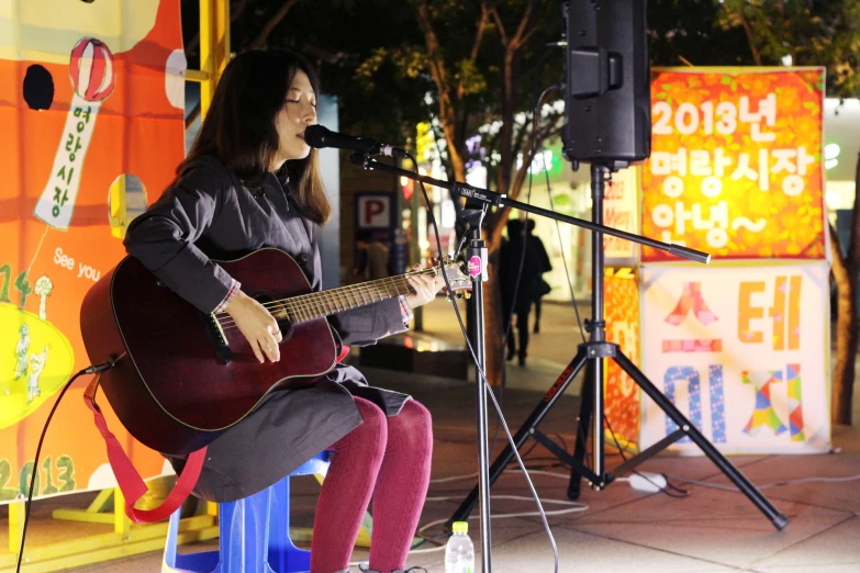 a woman plays guitar on a stool in front of an open air stage