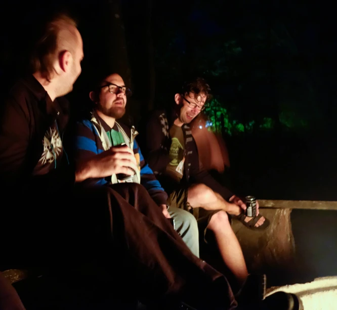 three people are sitting together outside in the dark