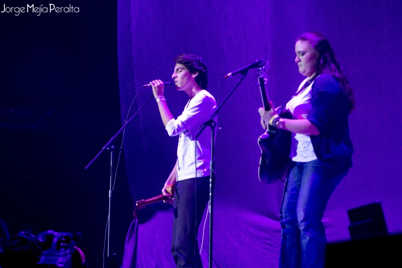 two people standing in front of microphones on stage