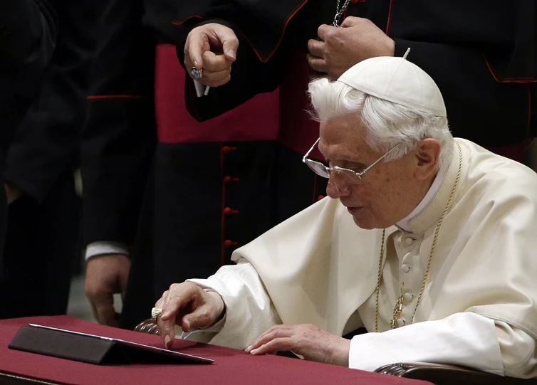 pope in white glasses sitting down at a desk
