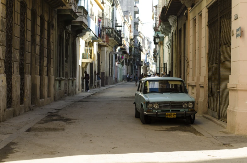 an old blue car sits in the middle of the alley way