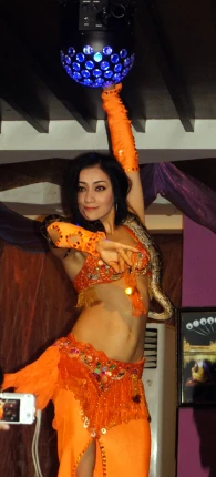a belly dancer in orange holds a large ball