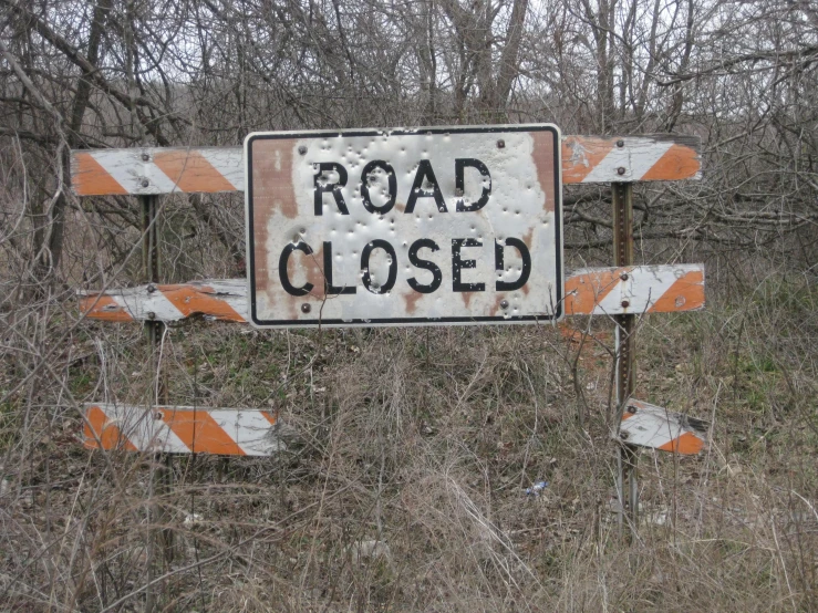 an old sign that reads road closed is set up in the woods