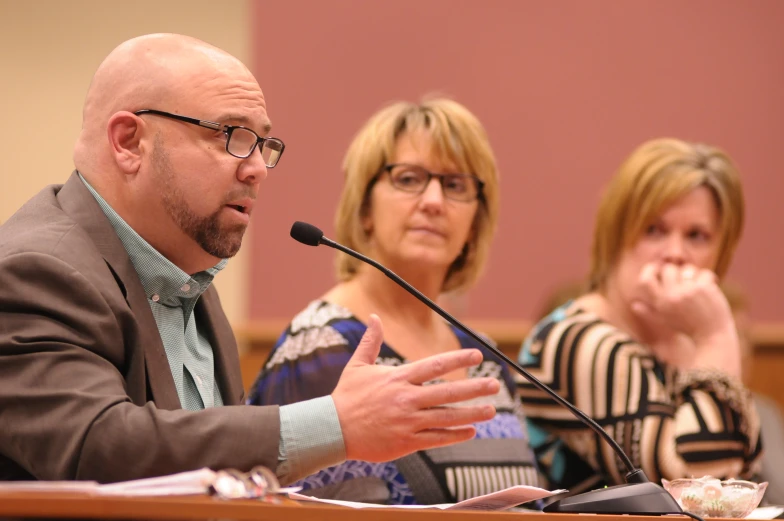 three people sitting down and one person standing up giving a speech