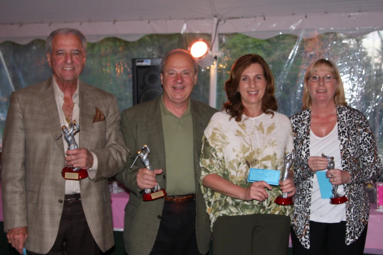 four people holding trophies standing in front of a curtain