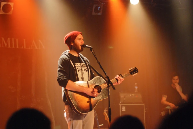 man singing into a microphone on stage with a guitar