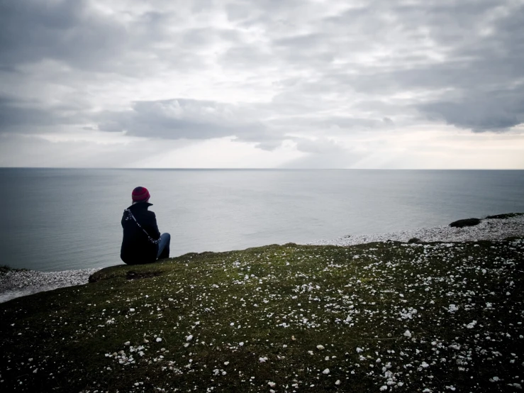 man sitting on a grassy hill overlooking the ocean