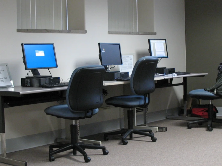 three laptops, one with a monitor and mouse, sit on three black chairs