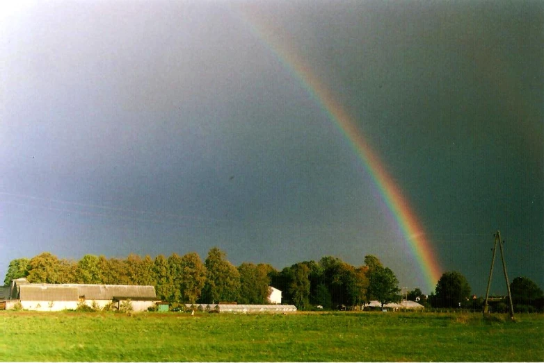 a large field with a rainbow and a barn
