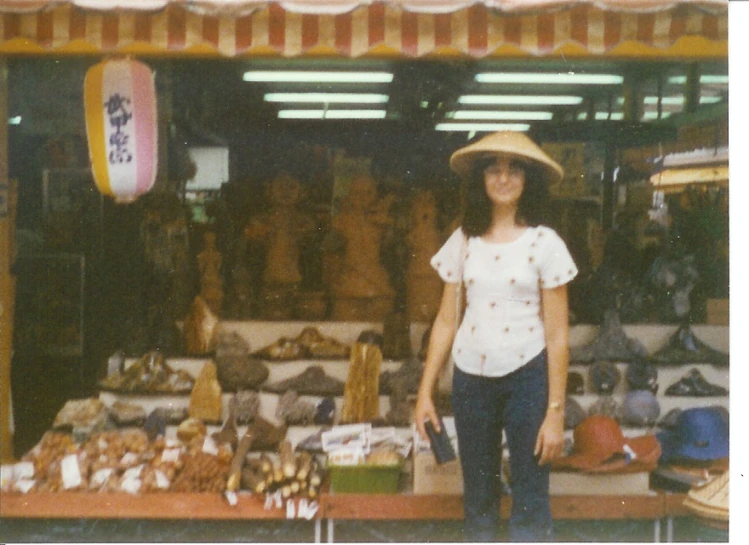 woman in white shirt and hat standing outside of market